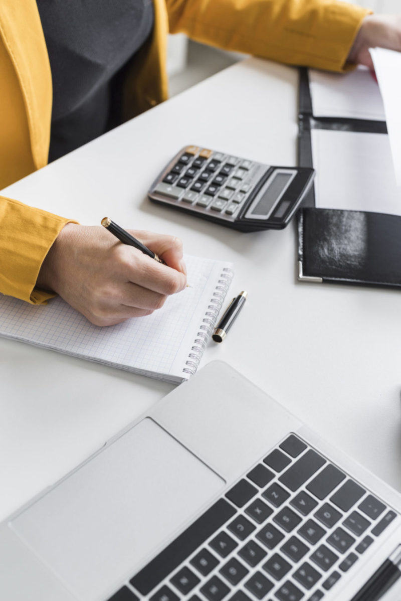 Personne écrivant avec calculatrice et ordinateur portable.